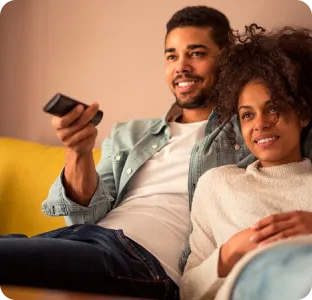 Casal sorridente assistindo televisão juntos no sofá.