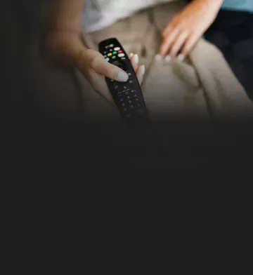 Pessoa segurando um controle remoto, sentada com uma manta sobre as pernas.